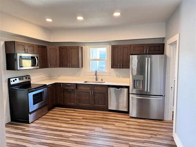 kitchen with a sink, dark brown cabinets, appliances with stainless steel finishes, light countertops, and light wood-type flooring