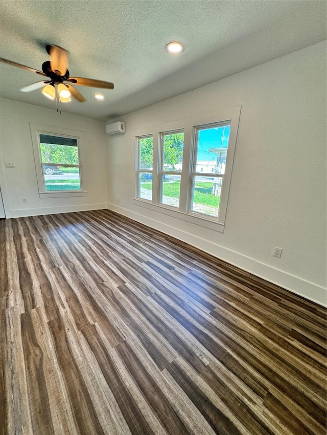 spare room featuring a wall unit AC, a ceiling fan, a textured ceiling, wood finished floors, and baseboards