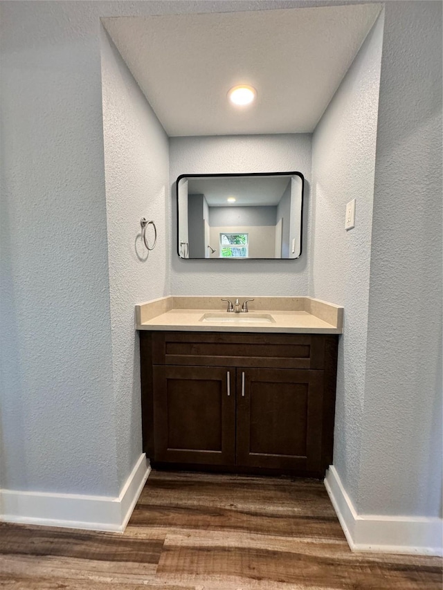 bathroom featuring a textured wall, vanity, baseboards, and wood finished floors