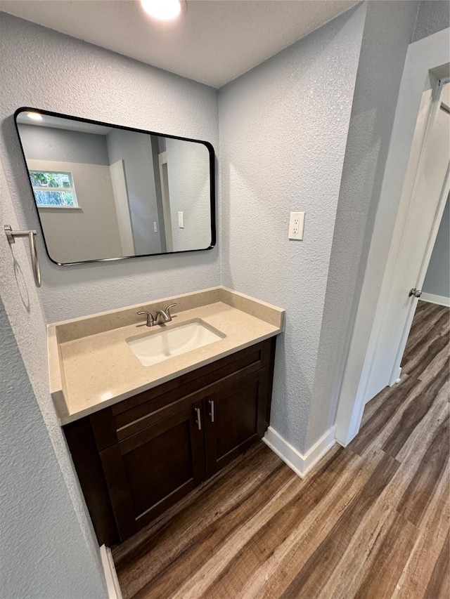 bathroom featuring vanity, baseboards, wood finished floors, and a textured wall