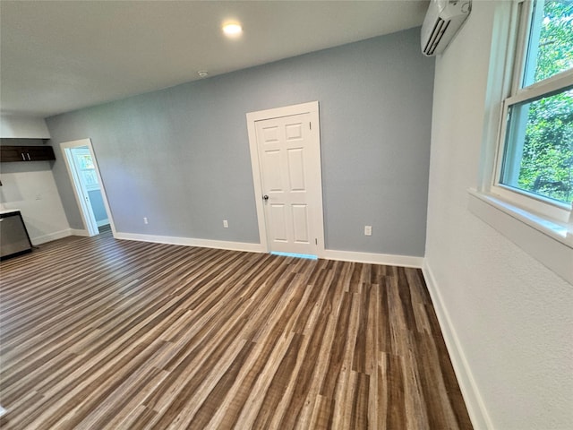 unfurnished room with recessed lighting, dark wood-style flooring, a wall unit AC, and baseboards