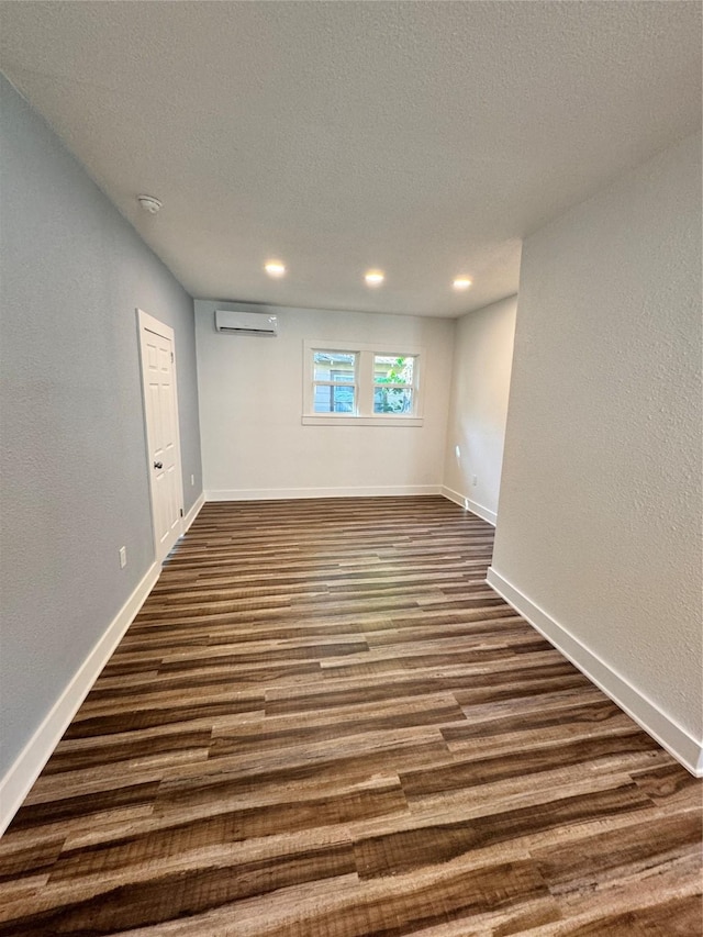 unfurnished room with a wall unit AC, a textured ceiling, baseboards, and dark wood-type flooring