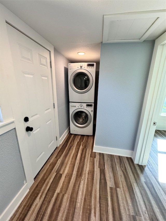 laundry area with a textured wall, laundry area, wood finished floors, baseboards, and stacked washer / drying machine