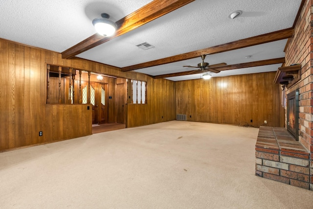 unfurnished living room with beam ceiling, wood walls, light colored carpet, a textured ceiling, and a fireplace