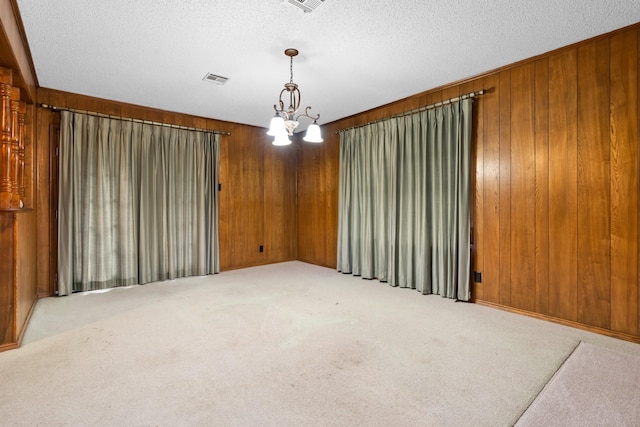 spare room with a chandelier, light carpet, a textured ceiling, and wooden walls