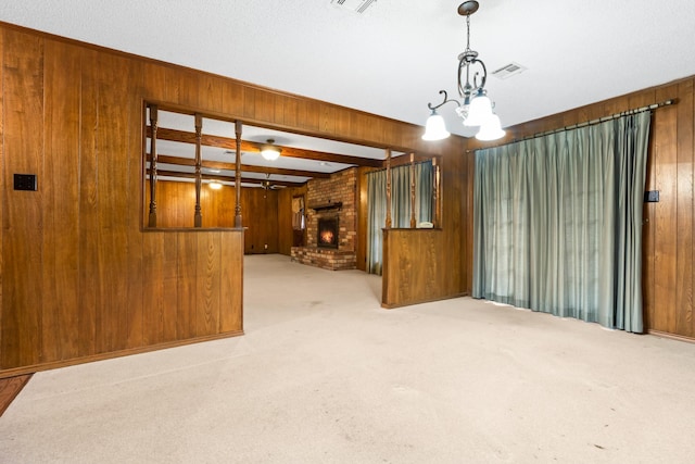 spare room featuring a brick fireplace, light colored carpet, wooden walls, beam ceiling, and a chandelier