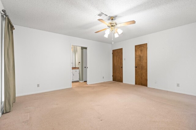 unfurnished bedroom with ceiling fan, light colored carpet, a textured ceiling, and ensuite bath