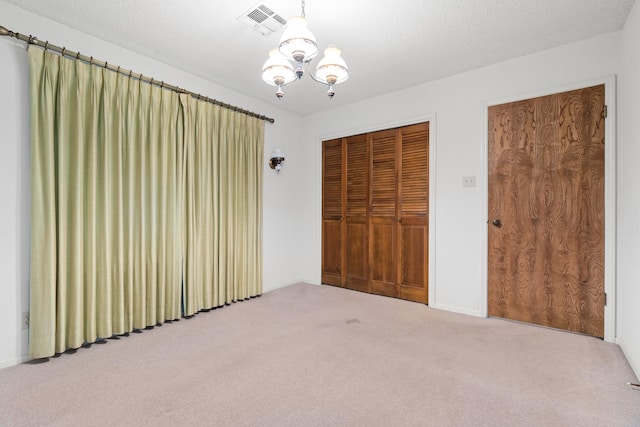 unfurnished bedroom with carpet, a notable chandelier, a textured ceiling, and a closet