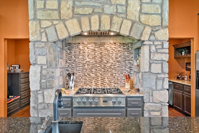 kitchen with dark stone counters, sink, stainless steel gas stovetop, and dark wood-type flooring