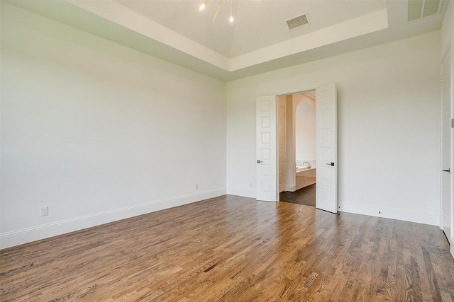 empty room featuring visible vents, a raised ceiling, baseboards, and wood finished floors