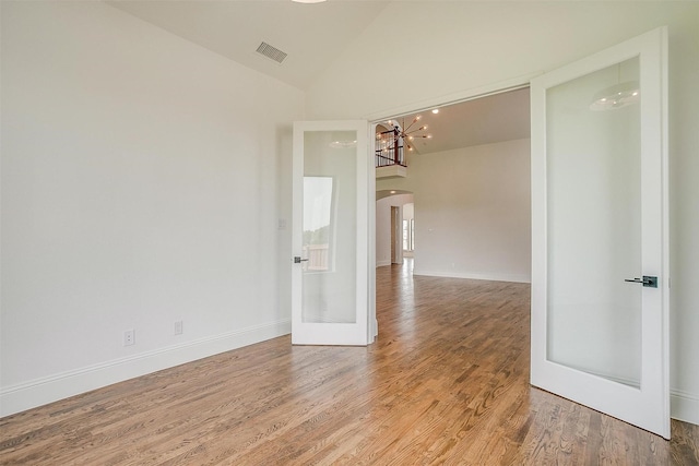 empty room featuring visible vents, baseboards, light wood-style flooring, arched walkways, and high vaulted ceiling