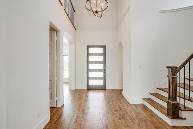 entryway featuring wood finished floors, baseboards, arched walkways, stairs, and a chandelier