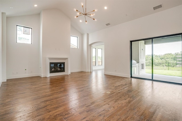 unfurnished living room featuring visible vents, wood finished floors, arched walkways, and a glass covered fireplace