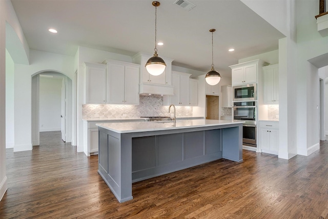 kitchen featuring white cabinets, stainless steel appliances, a center island with sink, and dark wood-type flooring