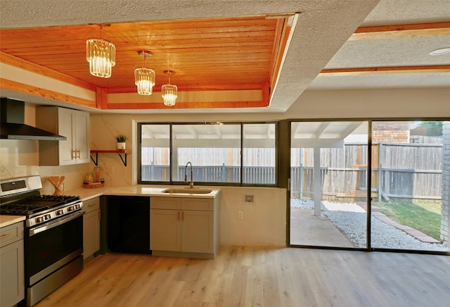 kitchen featuring gas range, a tray ceiling, wall chimney range hood, pendant lighting, and dishwasher