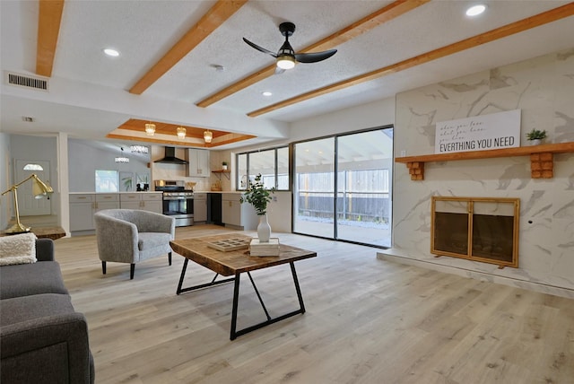 living room featuring light hardwood / wood-style flooring, ceiling fan, a fireplace, a textured ceiling, and beamed ceiling