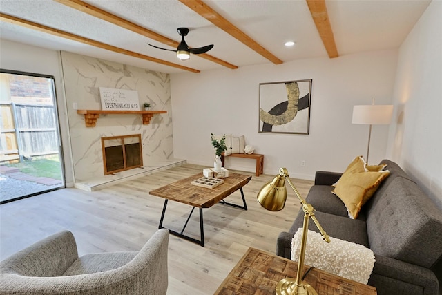 living room featuring beamed ceiling, ceiling fan, light wood-type flooring, and a fireplace