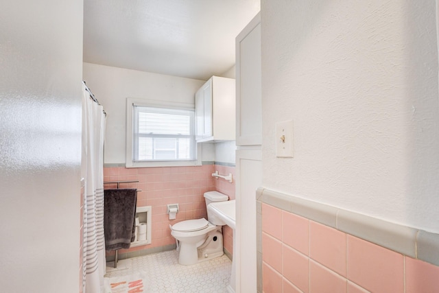 bathroom with toilet, tile patterned floors, and tile walls