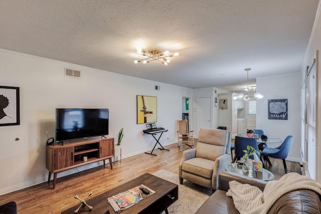 living room featuring crown molding, light hardwood / wood-style flooring, a chandelier, and a textured ceiling