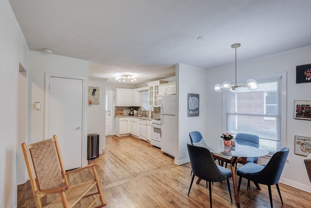 dining room featuring ornamental molding, light wood-type flooring, a notable chandelier, and sink