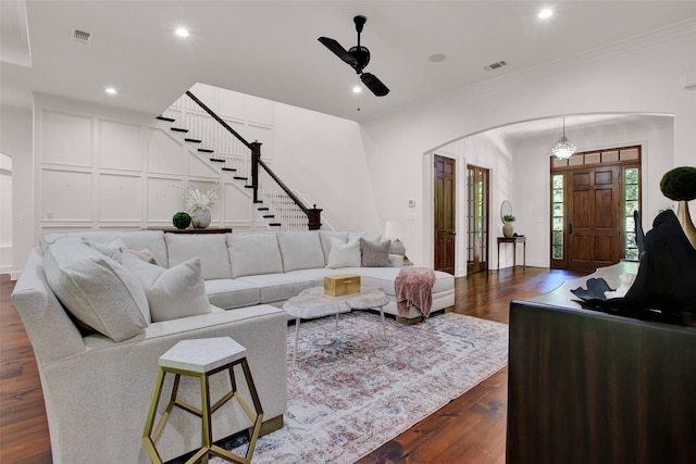 living area with arched walkways, visible vents, stairs, dark wood finished floors, and crown molding