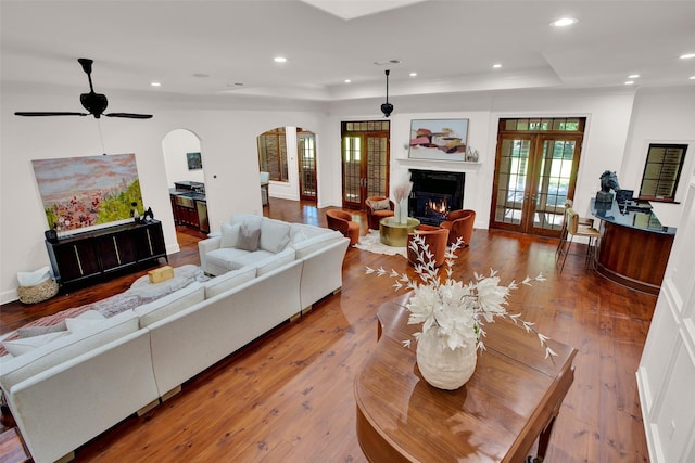 living area featuring arched walkways, a high end fireplace, french doors, hardwood / wood-style floors, and a raised ceiling