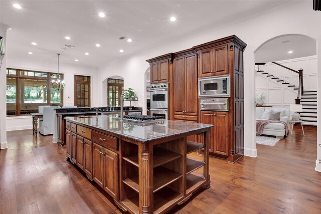 kitchen featuring a chandelier, stainless steel appliances, a center island with sink, hardwood / wood-style floors, and dark stone countertops