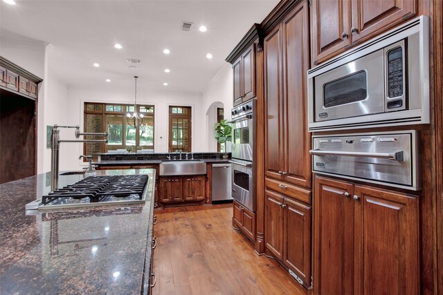 kitchen featuring dark stone counters, light hardwood / wood-style flooring, stainless steel appliances, hanging light fixtures, and sink