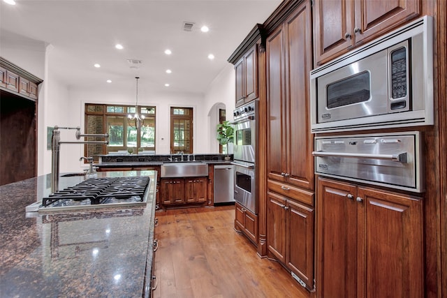 kitchen with arched walkways, a sink, light wood-style floors, appliances with stainless steel finishes, and a warming drawer