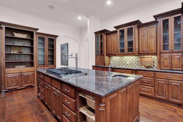 kitchen featuring tasteful backsplash, a center island with sink, stainless steel gas stovetop, sink, and ornamental molding