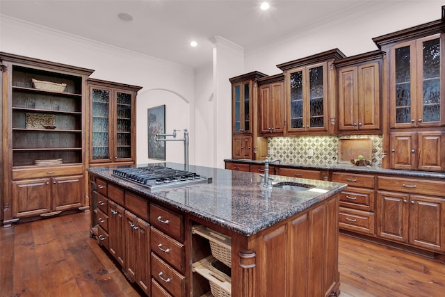 kitchen with stainless steel gas cooktop, a sink, open shelves, an island with sink, and dark wood finished floors