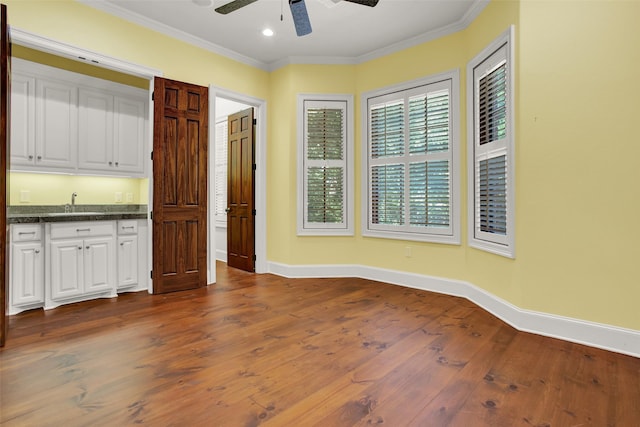 unfurnished room featuring dark wood finished floors, a sink, crown molding, and baseboards