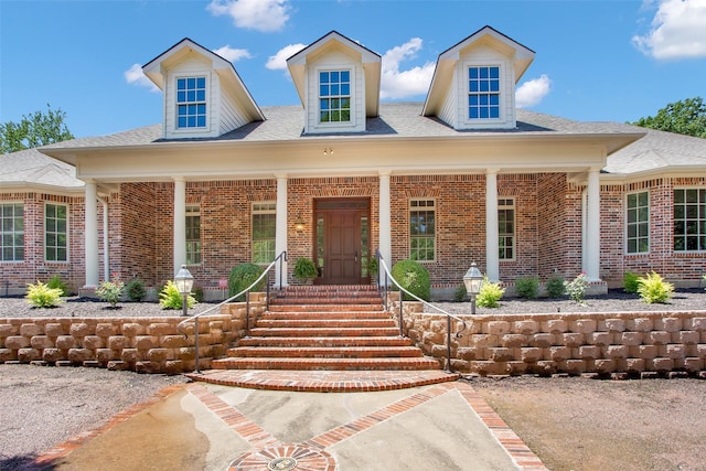 view of front of property with a shingled roof, covered porch, and brick siding