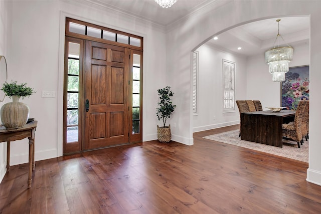 foyer featuring baseboards, arched walkways, ornamental molding, hardwood / wood-style floors, and an inviting chandelier