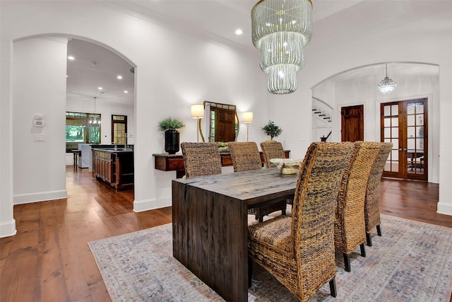 dining room with baseboards, arched walkways, hardwood / wood-style flooring, crown molding, and a notable chandelier