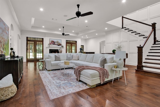 living room featuring arched walkways, a decorative wall, a lit fireplace, and a tray ceiling