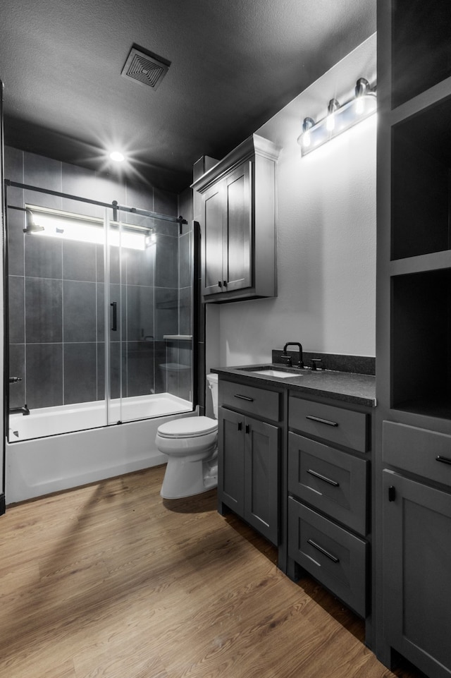 full bathroom featuring a textured ceiling, hardwood / wood-style flooring, toilet, vanity, and bath / shower combo with glass door