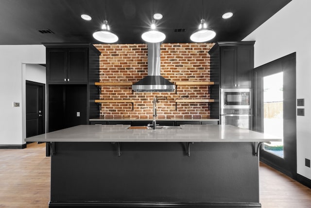 kitchen featuring an island with sink, stainless steel appliances, decorative light fixtures, and light hardwood / wood-style floors