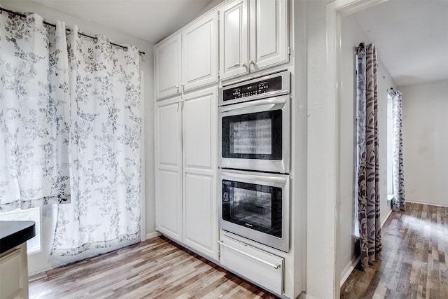 kitchen featuring double oven, a wealth of natural light, light hardwood / wood-style floors, and white cabinets