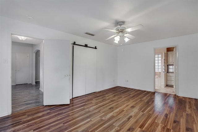 unfurnished bedroom with dark hardwood / wood-style flooring, connected bathroom, a barn door, and ceiling fan