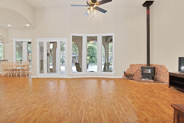 unfurnished living room featuring a high ceiling, hardwood / wood-style flooring, a wood stove, and a wealth of natural light