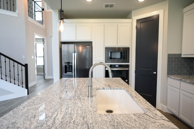 kitchen with sink, light stone counters, hanging light fixtures, appliances with stainless steel finishes, and white cabinets