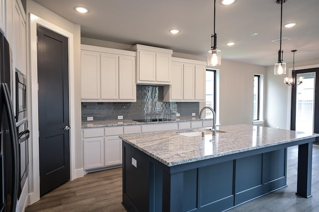 kitchen featuring white cabinets, hanging light fixtures, light stone counters, black appliances, and a center island with sink