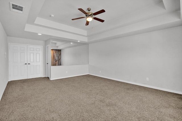 unfurnished bedroom with a tray ceiling, carpet flooring, ceiling fan, and a closet