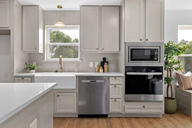 kitchen with pendant lighting, sink, stainless steel appliances, and light hardwood / wood-style flooring