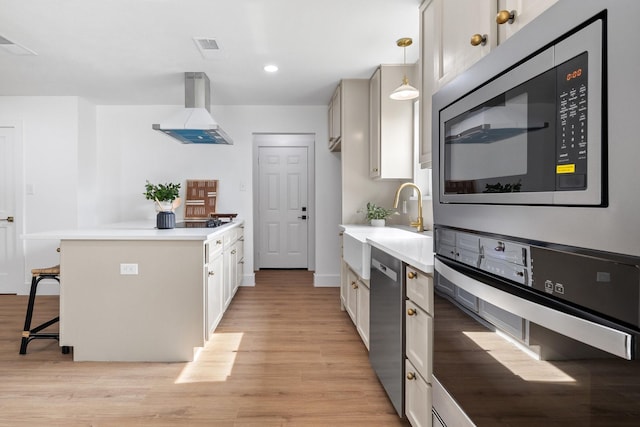 kitchen with a kitchen bar, stainless steel appliances, wall chimney range hood, pendant lighting, and light hardwood / wood-style flooring