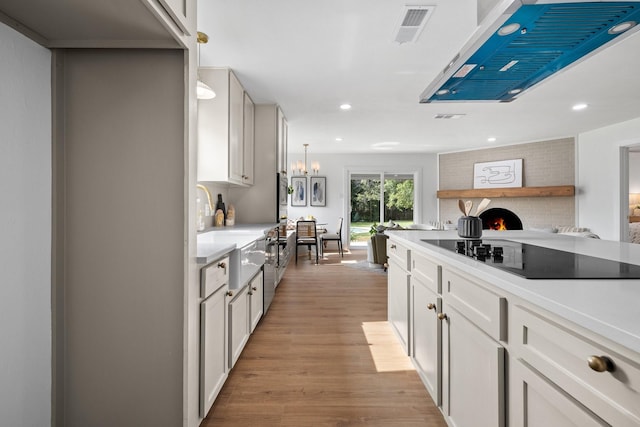 kitchen featuring white cabinets, black electric stovetop, light wood-type flooring, and hanging light fixtures