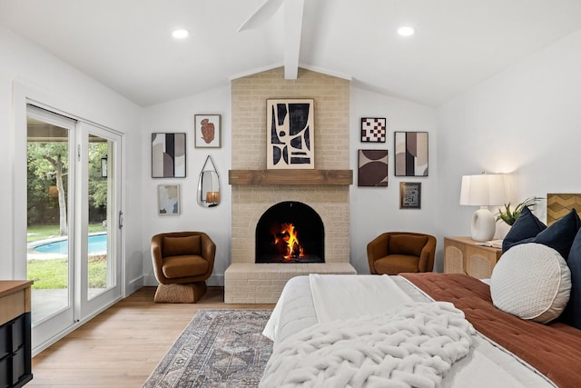 bedroom featuring access to exterior, light hardwood / wood-style flooring, a fireplace, and vaulted ceiling with beams