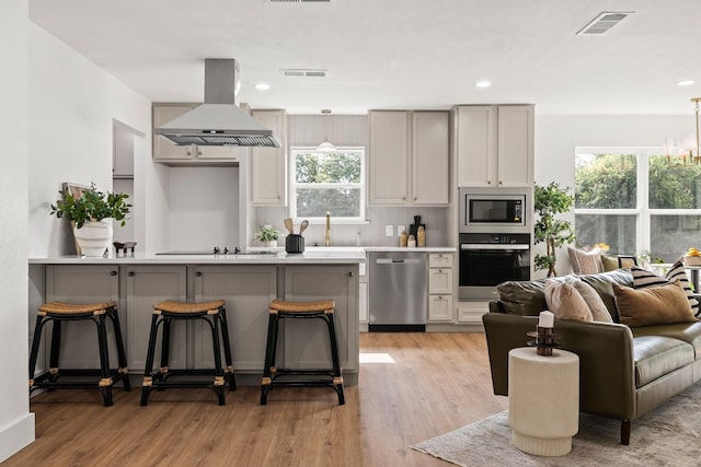 kitchen with appliances with stainless steel finishes, extractor fan, light hardwood / wood-style flooring, gray cabinets, and a breakfast bar area