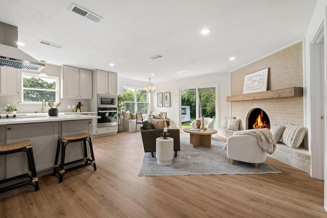 living room with a chandelier, light wood-type flooring, and a brick fireplace